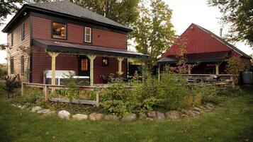 A rustic two-story house with a porch and a red barn in the background.