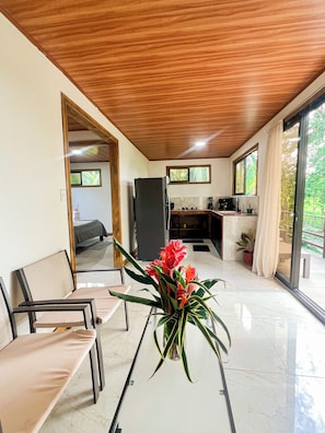A modern interior with a dining area, a kitchen, and a view of greenery.