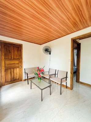 A room with a wooden ceiling, a fan, a table with chairs, and a door.