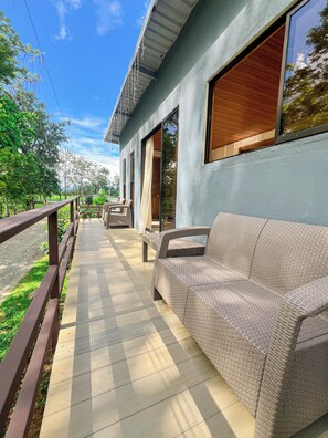 A covered outdoor area with a wicker sofa, a wooden bench, and a railing.
