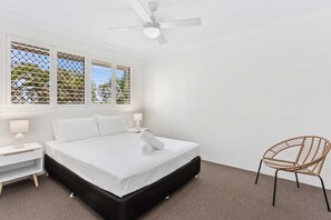 A bedroom with a bed, nightstands, a chair, a ceiling fan, and a window with blinds. - Miami Resort Living - Two Bedroom Resort Views (Gold Coast)