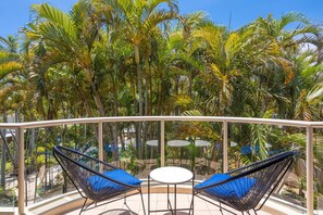 A balcony with two chairs and a table, surrounded by palm trees. - Miami Resort Living - Two Bedroom Resort Views (Gold Coast)