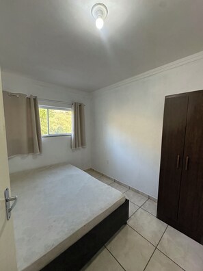 A room with a bed, a window with curtains, a wardrobe, and a ceiling light. - Chácara JM: Your little corner to connect with nature and enjoy days of leisure. (Lindóia)