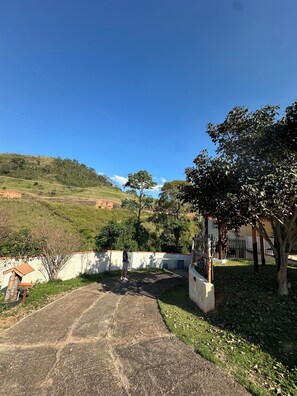 A paved pathway leading to a building with a white wall and a tree in the foreground. - Chácara JM: Your little corner to connect with nature and enjoy days of leisure. (Lindóia)