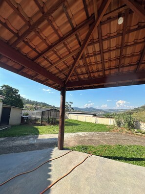 A covered outdoor area with a concrete floor, a metal roof, and a view of distant hills. - Chácara JM: Your little corner to connect with nature and enjoy days of leisure. (Lindóia)