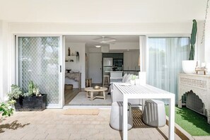 A modern living space with a sliding glass door leading to a kitchen, a dining area with a white table, and a small seating area with a round table. - Calm @ Noosa centrally located on iconic Noosa Parade (Noosa Heads)