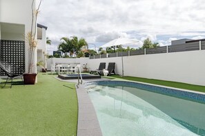 A swimming pool with a surrounding deck, a white fence, and a lounge area with chairs and umbrellas. - Calm @ Noosa centrally located on iconic Noosa Parade (Noosa Heads)