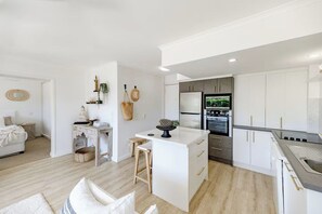 A modern kitchen with white cabinetry, a central island, and a built-in oven. - Calm @ Noosa centrally located on iconic Noosa Parade (Noosa Heads)