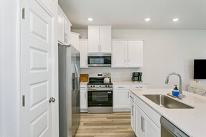 A modern kitchen with white cabinetry, stainless steel appliances, and a wooden floor. - Pool & Playground - Newly Built 3BR Gulf Breeze Townhome Near The Zoo, Navarre Beach, and Pensacola (Gulf Breeze)