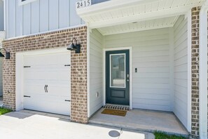 A residential building with a white garage door, a dark front door, and a brick facade. - Pool & Playground - Newly Built 3BR Gulf Breeze Townhome Near The Zoo, Navarre Beach, and Pensacola (Gulf Breeze)