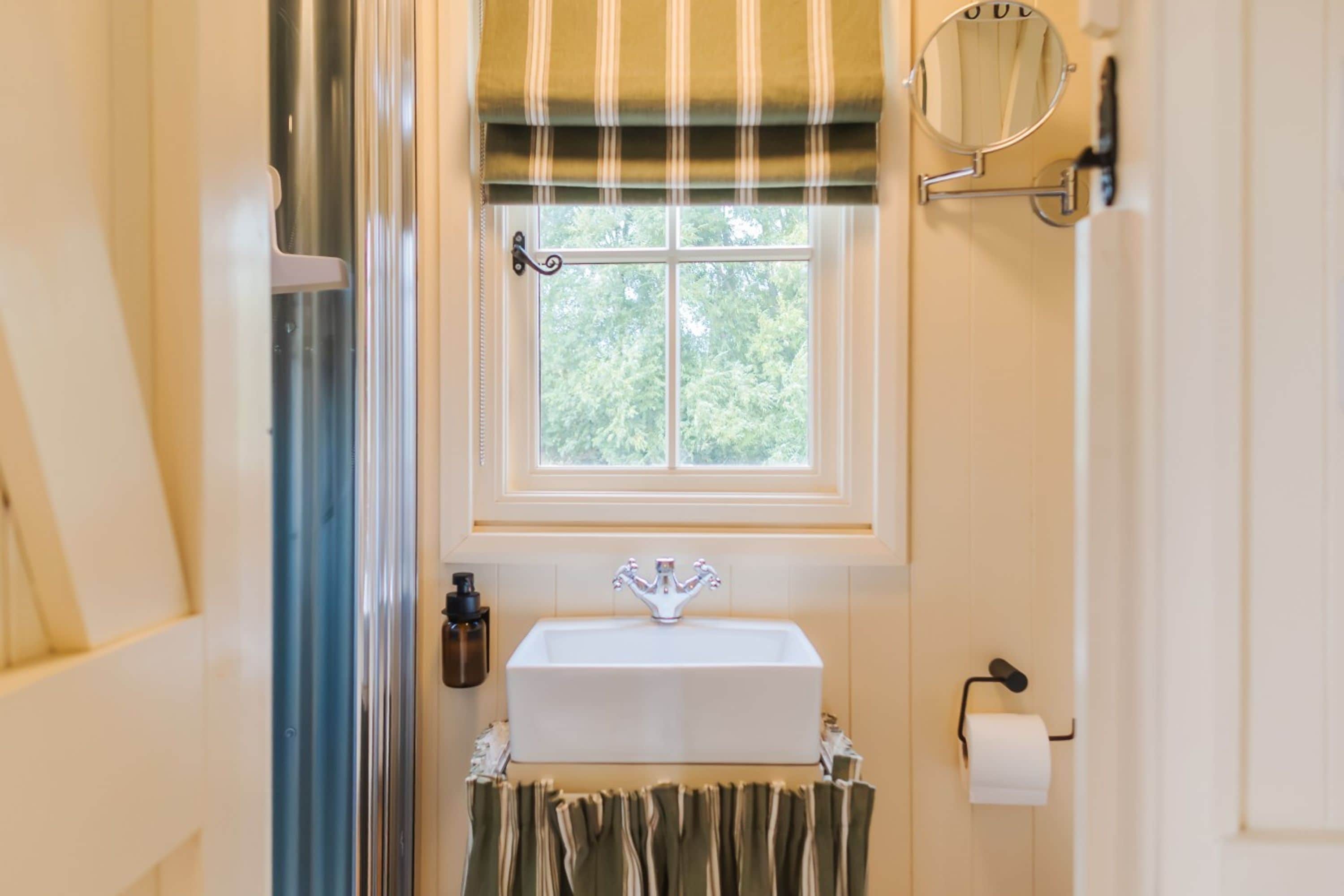 Een badkamer met een raam, een wastafel, een spiegel en een toiletrolhouder.