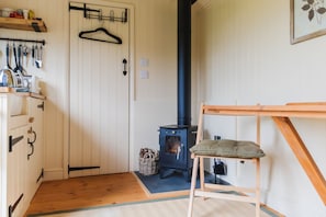 Quarto com piso de madeira, fogão preto, uma cadeira e porta com porta-roupas.