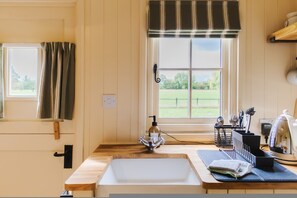Cozinha com bancada de madeira, pia, janela com cortinas e vista para um campo verde.