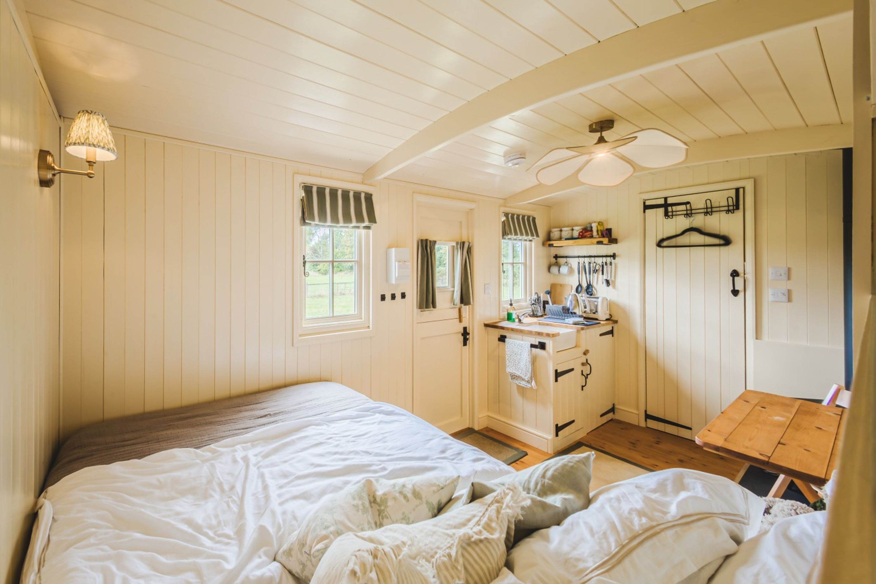 A bedroom with a large bed, a small desk, and a kitchenette area.