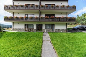 Un edifici de dues plantes amb façana de pedra, entrada enjardinada i un cotxe a la zona d'aparcament.