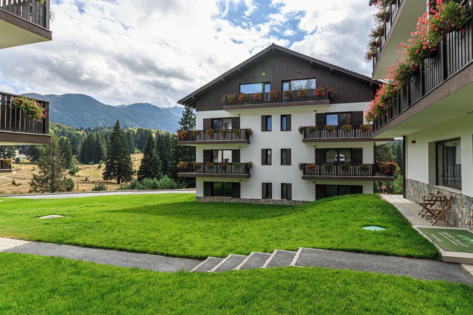 A multi-story building with balconies, a grassy courtyard, and a mountainous backdrop.