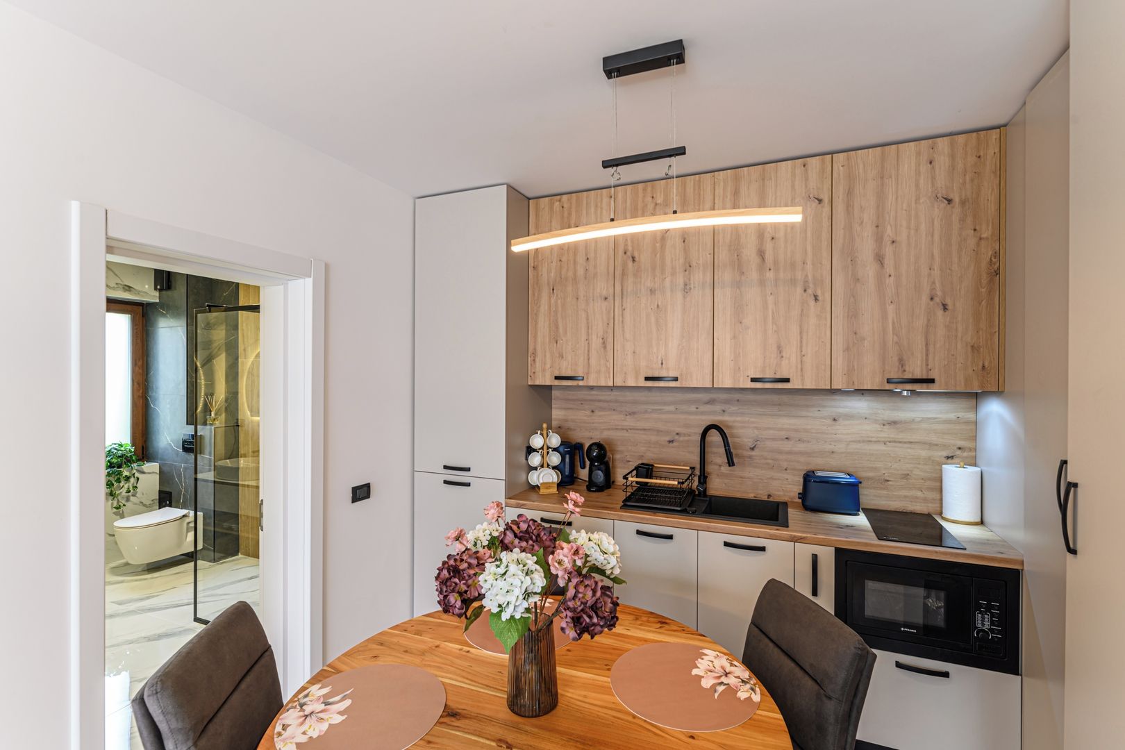 Una cocina moderna con armarios de madera, horno empotrado y un comedor con mesa y sillas redondas.