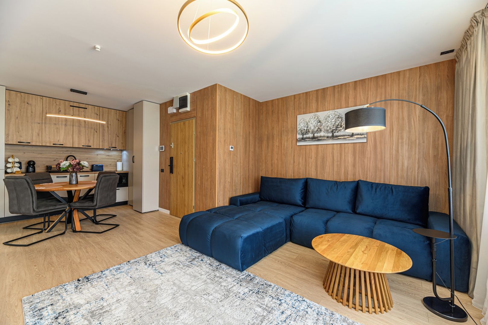 Una sala de estar moderna con un sofá modular, una mesa de centro redonda y un comedor con mesa y sillas de madera.