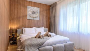A modern bedroom with a large bed, a bedside lamp, a wall-mounted artwork, and sheer curtains.