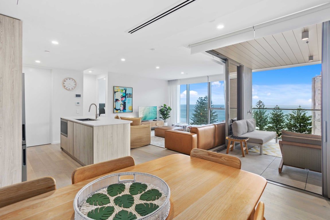 A modern kitchen with a central island, a dining area with a wooden table, and a living space with a sofa and armchairs.