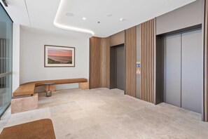 A modern lobby with a bench, a wall-mounted picture, a wooden panel wall, and a door with a control panel. - Luxury Ocean View Burleigh Apartment (Gold Coast)