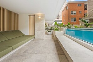 A modern interior with a green sofa, a pool, and a brick building in the background. - Luxury Ocean View Burleigh Apartment (Gold Coast)