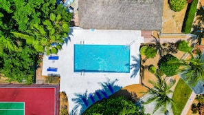 Eine Vogelperspektive eines Swimmingpools, umgeben von viel Grün und einem Tennisplatz.