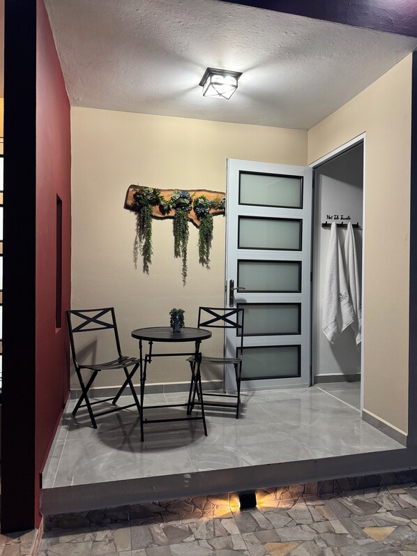 A room with a stone fireplace, a table with two chairs, a wall-mounted plant, and a door with a towel rack.