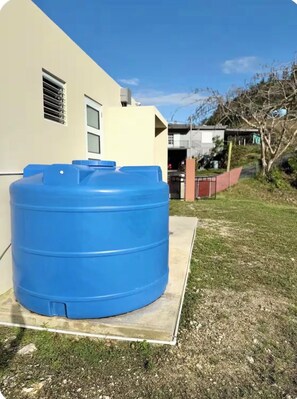 A large blue water tank outside a building with a paved area in front.