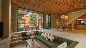 A spacious living area with a green sofa, wooden coffee table, and a view of a patio with outdoor furniture and plants. - Villa NAVAHO (Badung)