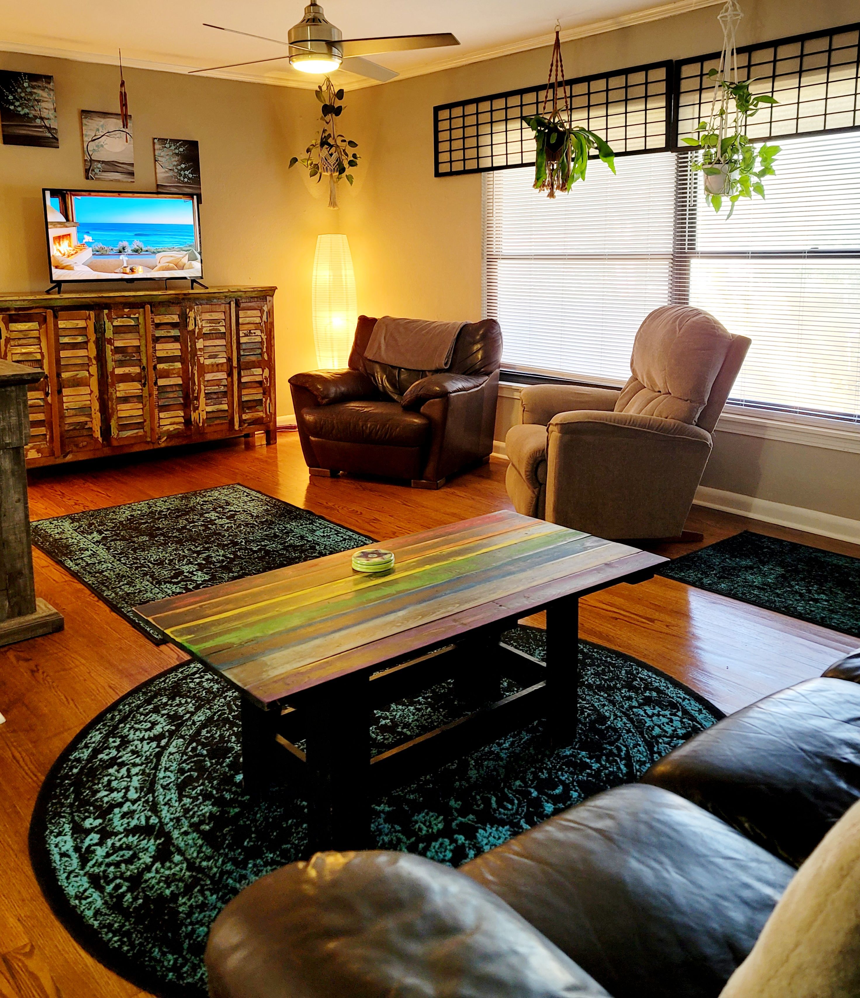 A living room with a sofa, two armchairs, a coffee table, a TV, a fireplace, and a window with blinds.
