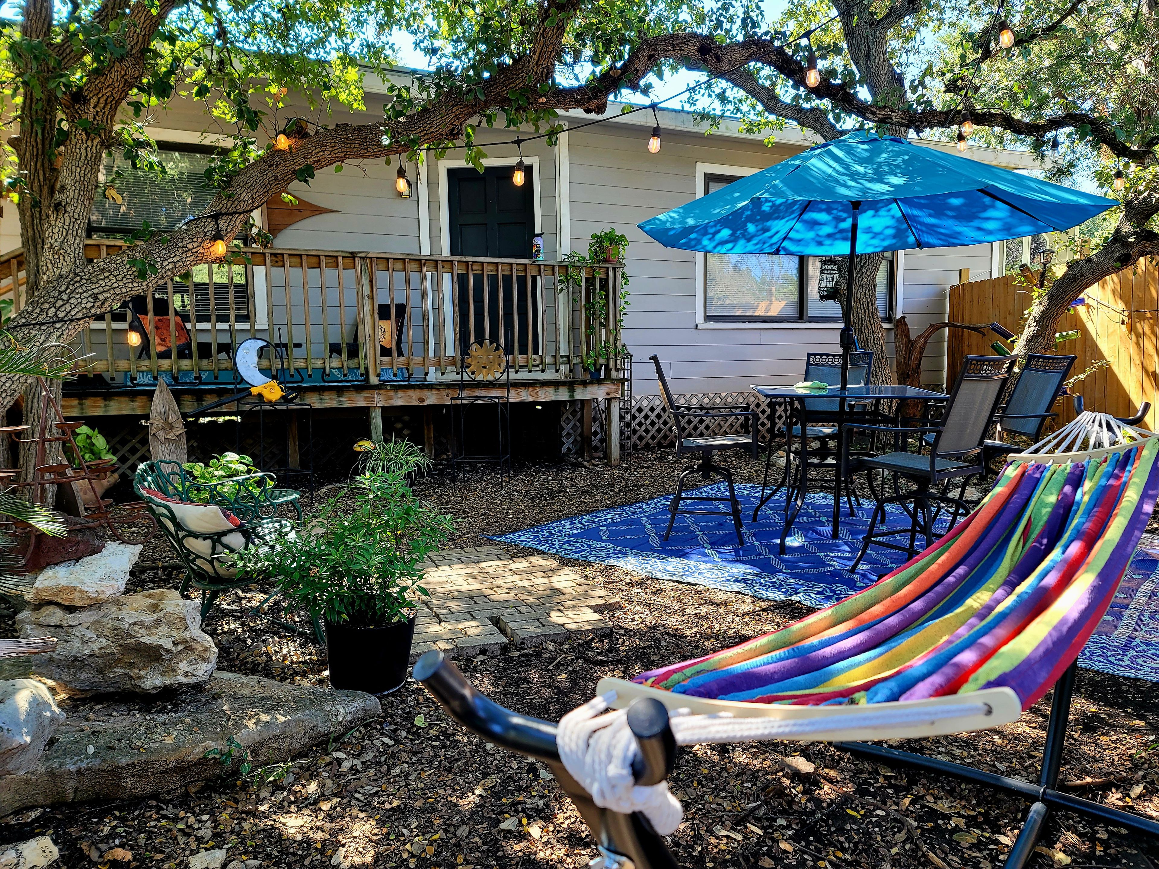 A backyard with a hammock, patio furniture, and a blue umbrella.