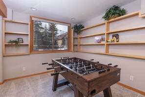 Een kamer met een tafelvoetbaltafel, houten planken en een raam met uitzicht op bomen.
