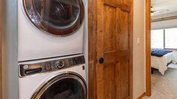 A laundry room with two front-loading washing machines and a wooden door leading to a bedroom.