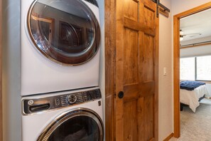 Una sala de bugaderia amb dues rentadores de càrrega frontal i una porta de fusta que dona a un dormitori.