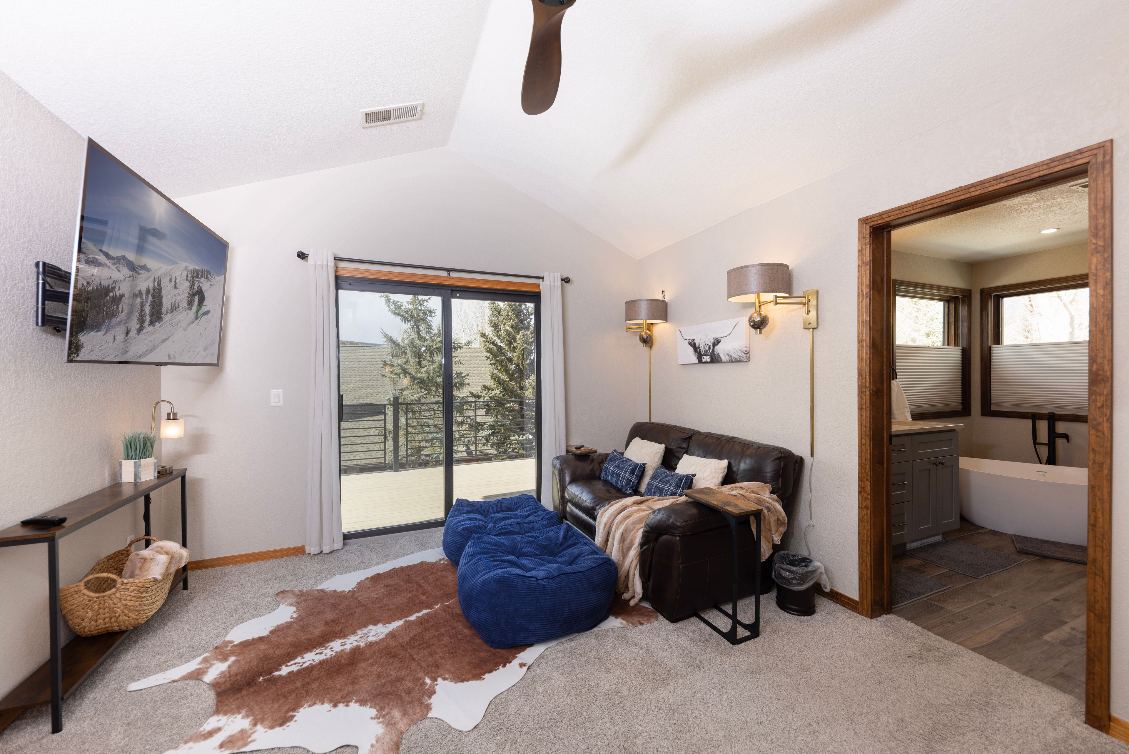 A spacious living room with a leather sofa, a large window, and a sliding glass door leading to a balcony.