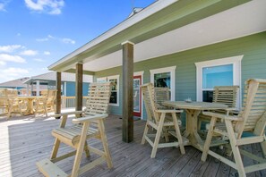 A wooden deck with outdoor furniture, a covered area, and a building with green siding and white trim. - Ocean View | Inflatable Hot Tub | Arcade Game (Crystal Beach)