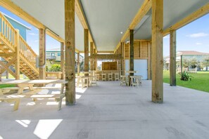 An outdoor covered patio area with wooden tables and benches, supported by wooden beams. - Ocean View | Inflatable Hot Tub | Arcade Game (Crystal Beach)