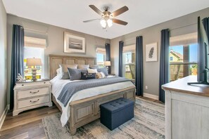 A bedroom with a bed, nightstands, a dresser, a ceiling fan, and a view of the outside. - Ocean View | Inflatable Hot Tub | Arcade Game (Crystal Beach)