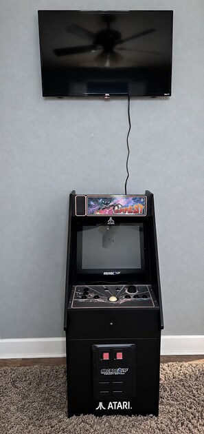 A gaming console with a screen, buttons, and a joystick, placed on a carpeted floor. - Ocean View | Inflatable Hot Tub | Arcade Game (Crystal Beach)