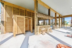 A wooden outdoor bar area with a thatched roof, wooden stools, and a concrete floor. - Ocean View | Inflatable Hot Tub | Arcade Game (Crystal Beach)