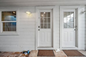 A white house with two doors and a window, a doormat, and a small trash bin. - Newly Built On the Beach Studio Loft with Views (Santa Monica)