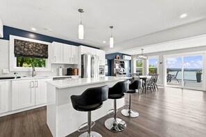 A modern kitchen with white cabinets, a large island, and bar stools. - Oceanfront Serenity Sauna (Halifax)
