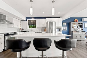 A modern kitchen with a central island, stainless steel appliances, and black bar stools. - Oceanfront Serenity Sauna (Halifax)