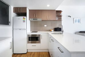 A modern kitchen with white cabinetry, a built-in oven, and a stainless steel refrigerator. - Sunseeker Studio - Ground Floor Apt (Noosa Heads)