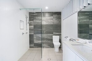 A modern bathroom with a glass shower enclosure, a white toilet, and a large mirror. - Sunseeker Studio - Ground Floor Apt (Noosa Heads)