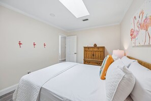 A bedroom with two beds, a wooden dresser, a door, and a wall with three flamingo decorations. - 3BR, 2BA home in Fernandina Beach's North End, on Amelia Island (Fernandina Beach)