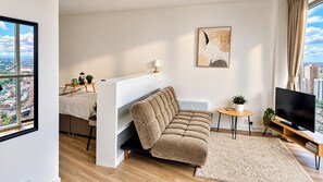 A modern living room with a sofa, a TV, a small table, and a view of the city through large windows. - Skyline Rotunda City Apartment I Bullring (Birmingham)