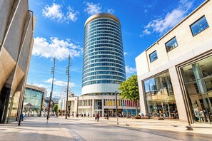A modern urban plaza with a prominent cylindrical building, pedestrian pathways, and surrounding commercial buildings. - Skyline Rotunda City Apartment I Bullring (Birmingham)