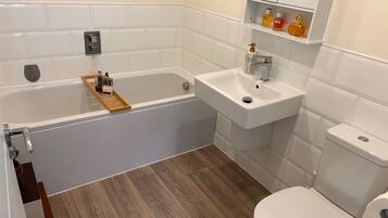 A bathroom with a bathtub, sink, toilet, and a wooden shelf with toiletries.